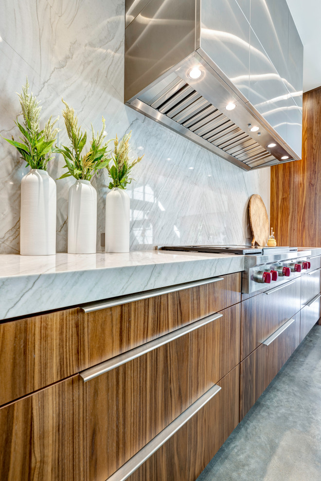 This is an example of a modern galley open plan kitchen in Houston with a single-bowl sink, flat-panel cabinets, medium wood cabinets, quartzite benchtops, beige splashback, stone slab splashback, panelled appliances, concrete floors, with island, grey floor, beige benchtop and exposed beam.