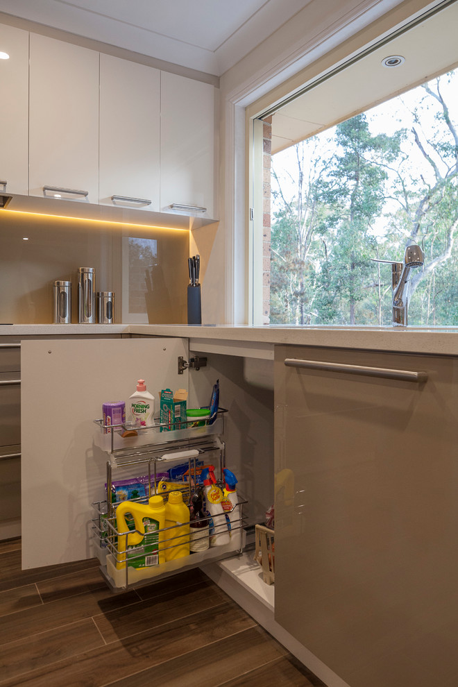 This is an example of an expansive contemporary u-shaped eat-in kitchen in Sydney with an undermount sink, flat-panel cabinets, green cabinets, quartz benchtops, brown splashback, glass sheet splashback, stainless steel appliances, ceramic floors and multiple islands.