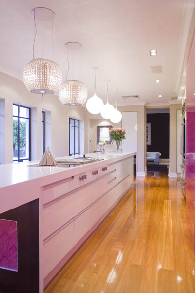 Large modern galley kitchen in Los Angeles with flat-panel cabinets, white cabinets, quartz benchtops, pink splashback, glass sheet splashback, stainless steel appliances, light hardwood floors and with island.