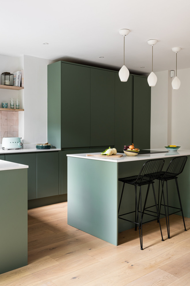 Große Moderne Küche in L-Form mit grünen Schränken, Laminat-Arbeitsplatte, Küchenrückwand in Rosa, Elektrogeräten mit Frontblende, hellem Holzboden, Kücheninsel und weißer Arbeitsplatte in London