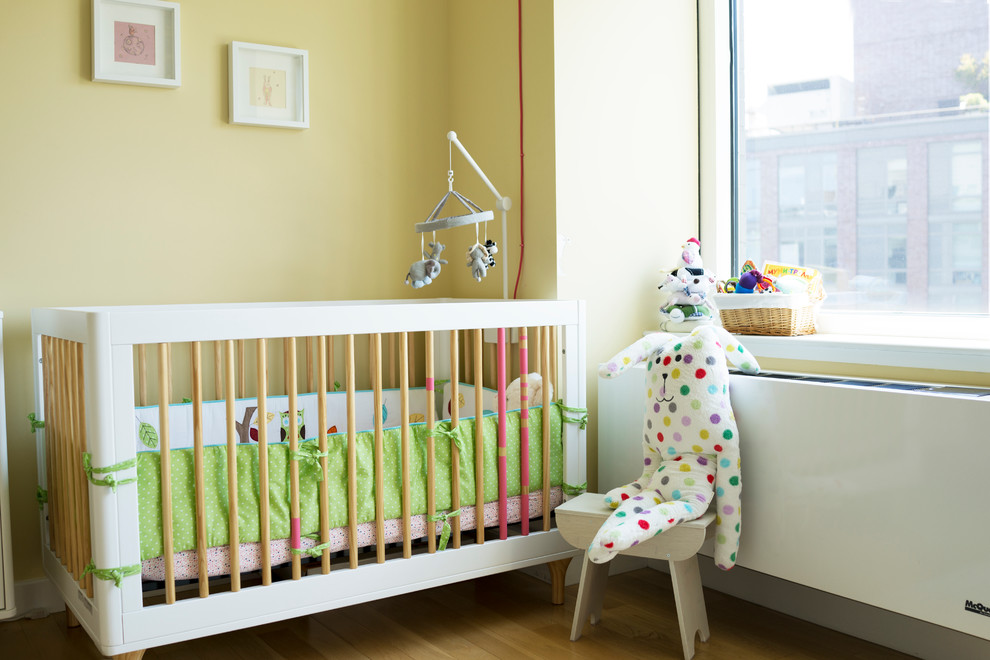 Design ideas for a scandinavian nursery for girls in New York with yellow walls and light hardwood floors.