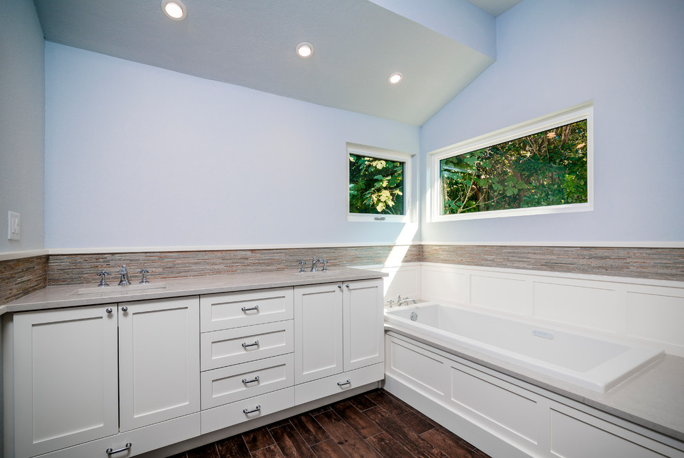 Drop-in bathtub - large transitional master beige tile and porcelain tile porcelain tile and brown floor drop-in bathtub idea with shaker cabinets, white cabinets, a one-piece toilet, blue walls, an undermount sink, quartz countertops and a hinged shower door