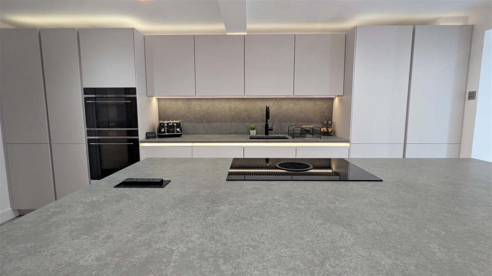 Inspiration for a large modern galley separate kitchen in Other with an integrated sink, white cabinets, quartzite benchtops, grey splashback, black appliances, with island and grey benchtop.
