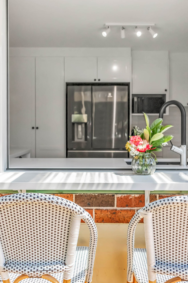 Design ideas for a mid-sized traditional u-shaped open plan kitchen in Sydney with an undermount sink, shaker cabinets, white cabinets, quartz benchtops, white splashback, subway tile splashback, stainless steel appliances, vinyl floors, a peninsula, brown floor and white benchtop.