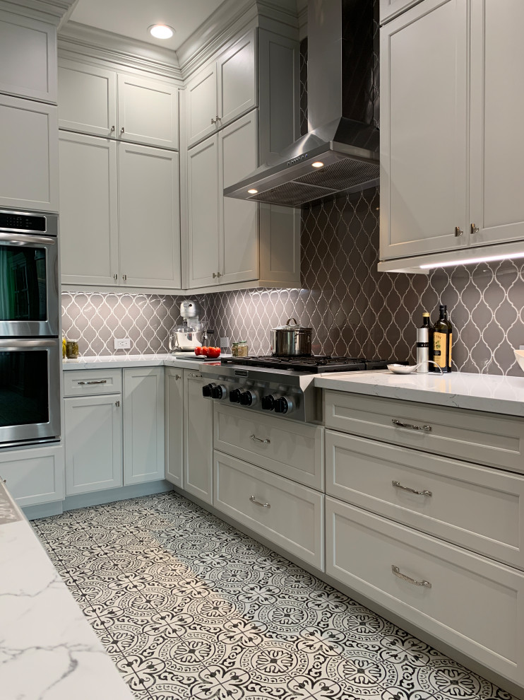 Example of a transitional l-shaped porcelain tile and multicolored floor kitchen design in Houston with a farmhouse sink, recessed-panel cabinets, white cabinets, quartz countertops, gray backsplash, ceramic backsplash, stainless steel appliances, an island and white countertops