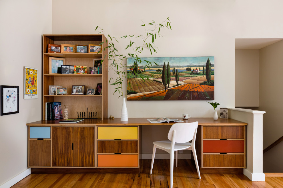 Small midcentury home office in Seattle with beige walls, medium hardwood floors, a built-in desk and brown floor.