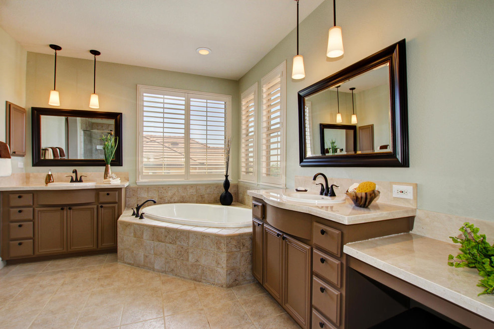 Photo of a mediterranean bathroom in Sacramento with a drop-in sink, flat-panel cabinets, brown cabinets, marble benchtops, a corner tub, limestone floors, beige floor and beige benchtops.