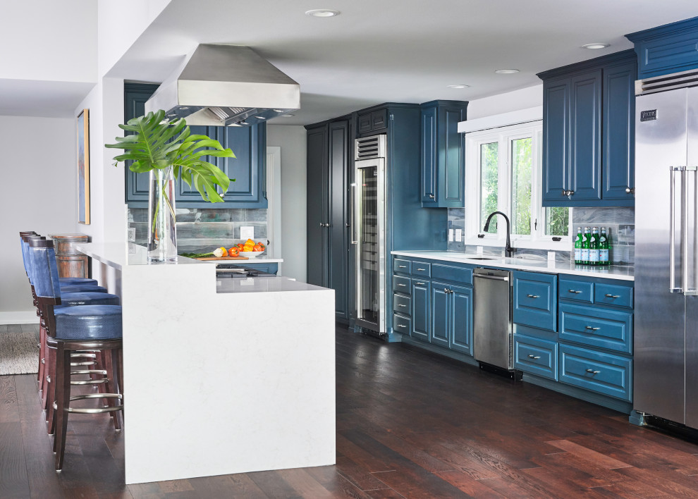 Kitchen - transitional galley dark wood floor and brown floor kitchen idea with an undermount sink, raised-panel cabinets, blue cabinets, gray backsplash, stainless steel appliances, a peninsula and white countertops