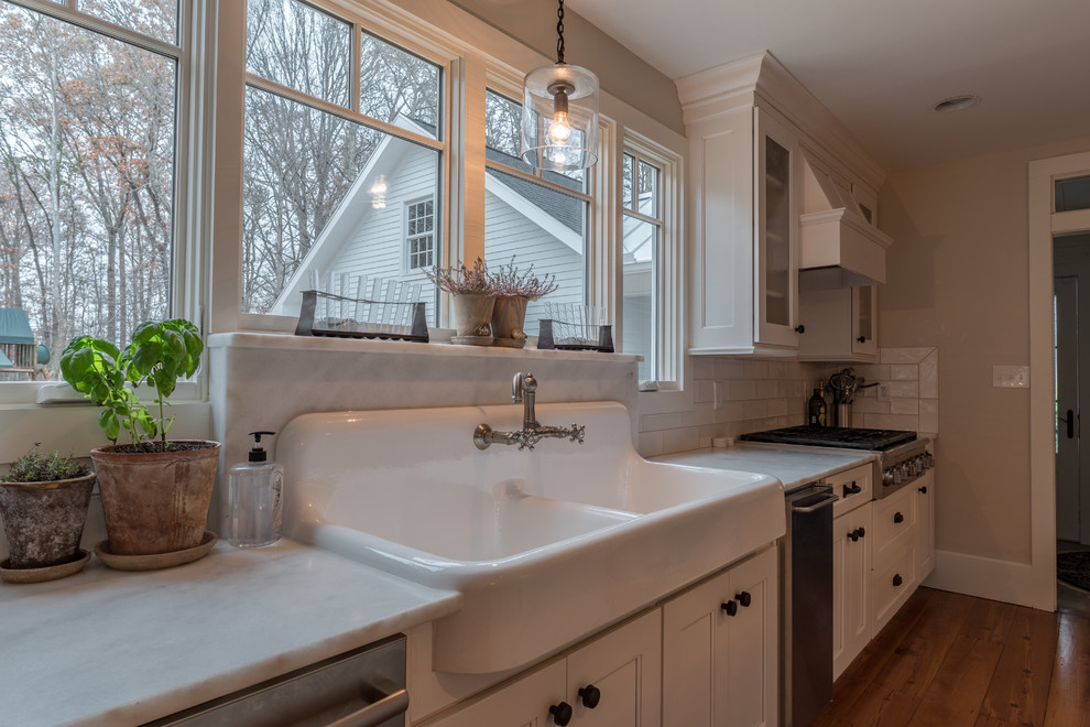 Mid-sized transitional medium tone wood floor kitchen photo with a farmhouse sink, recessed-panel cabinets, white cabinets, marble countertops, white backsplash, subway tile backsplash, stainless steel appliances and an island