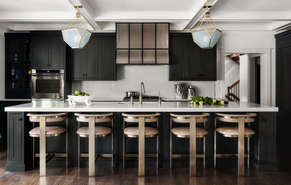 This is an example of a transitional l-shaped kitchen in Philadelphia with an undermount sink, black cabinets, white splashback, stone slab splashback, stainless steel appliances, dark hardwood floors, with island, brown floor, white benchtop and beaded inset cabinets.