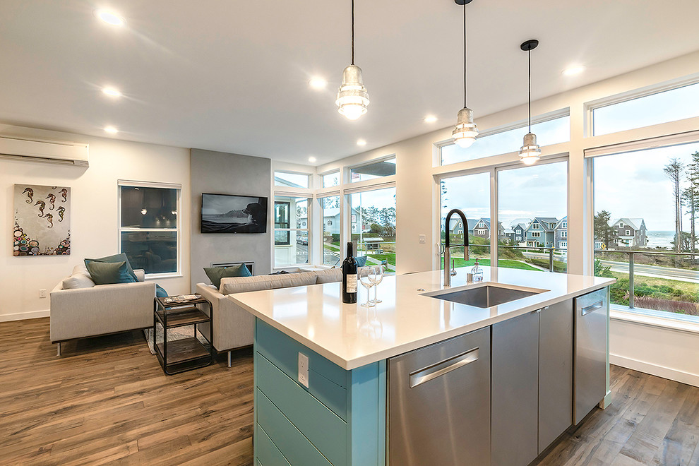 Mid-sized beach style l-shaped open plan kitchen in Seattle with an undermount sink, flat-panel cabinets, light wood cabinets, quartz benchtops, blue splashback, ceramic splashback, stainless steel appliances, medium hardwood floors, with island, brown floor and grey benchtop.
