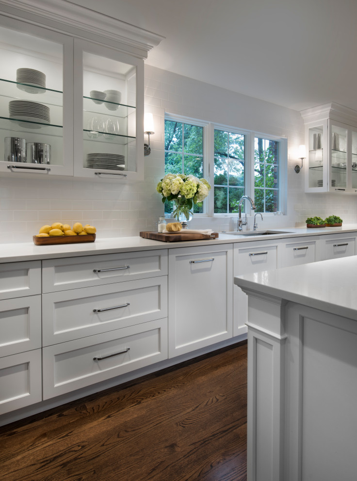 Inspiration for a large transitional galley brown floor kitchen remodel with an undermount sink, shaker cabinets, white cabinets, white backsplash, an island and white countertops