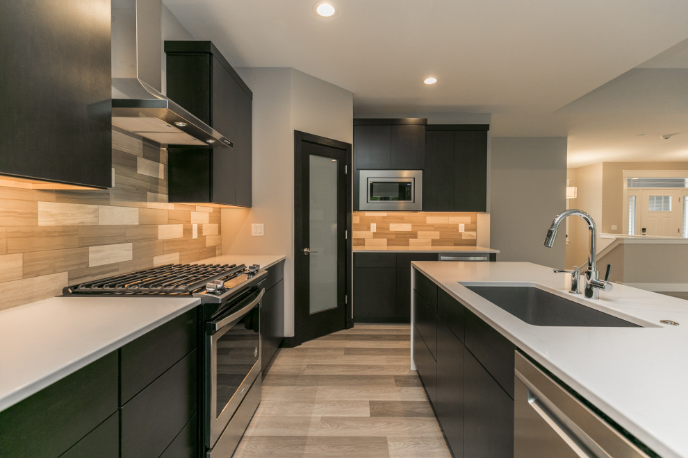 Example of a transitional galley gray floor open concept kitchen design in Cedar Rapids with flat-panel cabinets, black cabinets, beige backsplash, stainless steel appliances, an island and white countertops