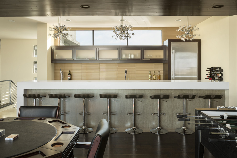 Design ideas for an expansive contemporary galley seated home bar in Las Vegas with glass-front cabinets, dark wood cabinets, beige splashback, dark hardwood floors, brown floor and white benchtop.