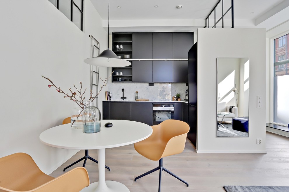 This is an example of a large contemporary l-shaped open plan kitchen in Gothenburg with flat-panel cabinets, black cabinets, white splashback, stone slab splashback, black appliances, light hardwood floors and no island.