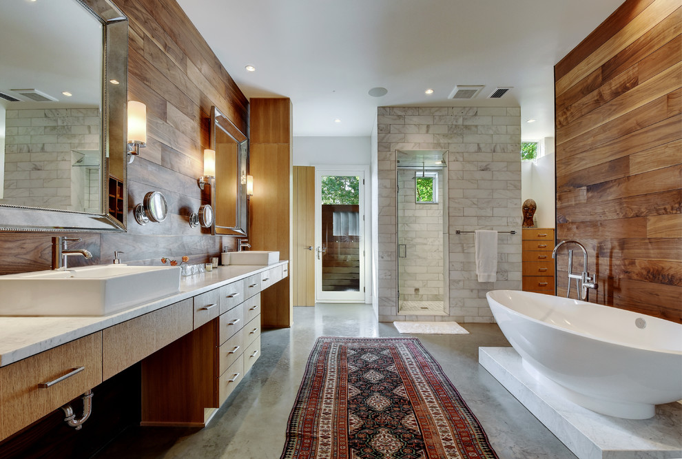 This is an example of a contemporary master bathroom in Austin with a vessel sink, flat-panel cabinets, light wood cabinets, marble benchtops, a freestanding tub, an alcove shower, white tile, brown walls and concrete floors.