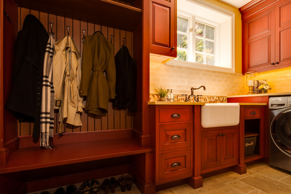 Mid-sized traditional l-shaped utility room in Seattle with a farmhouse sink, raised-panel cabinets, red cabinets, quartz benchtops, limestone floors, a side-by-side washer and dryer and orange walls.