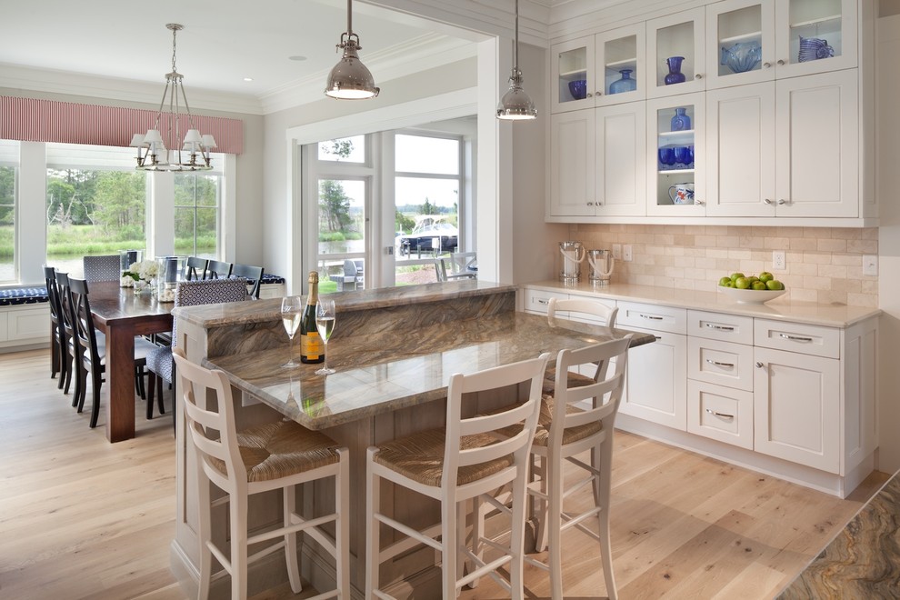 Large beach style u-shaped eat-in kitchen in DC Metro with recessed-panel cabinets, white cabinets, granite benchtops, beige splashback, stainless steel appliances, light hardwood floors, multiple islands and glass tile splashback.