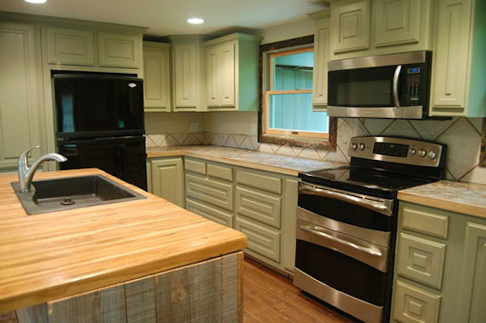 Mid-sized transitional l-shaped medium tone wood floor eat-in kitchen photo with a drop-in sink, raised-panel cabinets, green cabinets, wood countertops, ceramic backsplash, stainless steel appliances and an island