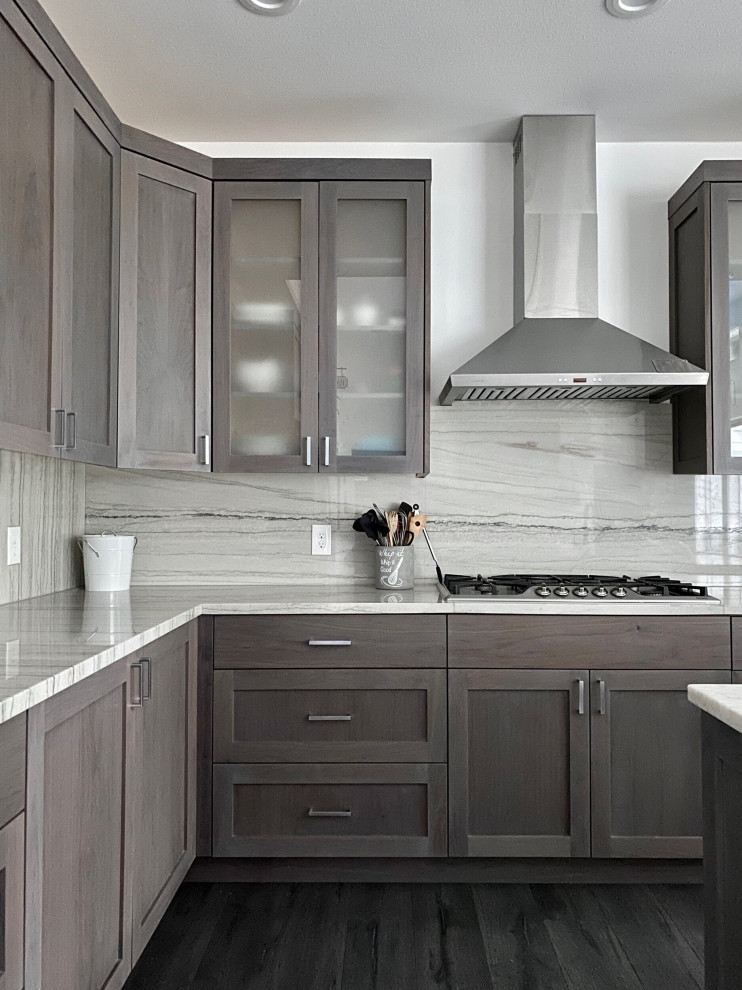 This is an example of a modern l-shaped open plan kitchen in Seattle with a farmhouse sink, raised-panel cabinets, brown cabinets, marble benchtops, white splashback, granite splashback, stainless steel appliances, vinyl floors, with island, brown floor and white benchtop.