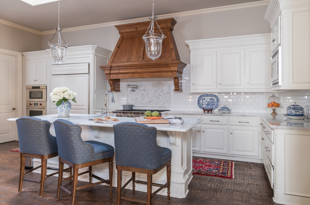 Inspiration for a large traditional u-shaped eat-in kitchen in Dallas with raised-panel cabinets, white cabinets, white splashback, stainless steel appliances, dark hardwood floors, with island, brown floor, marble benchtops and subway tile splashback.
