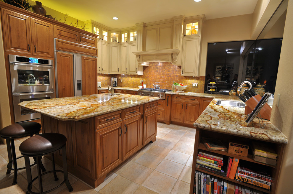 Inspiration for a transitional ceramic tile kitchen remodel with an undermount sink, raised-panel cabinets, distressed cabinets, granite countertops, metallic backsplash, metal backsplash, paneled appliances and an island