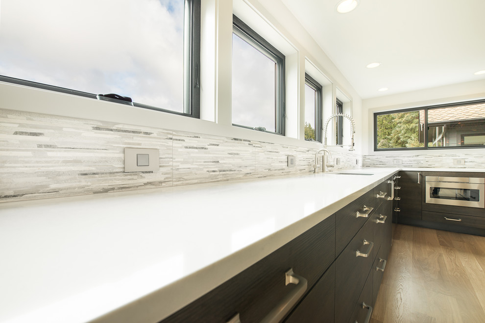 Large transitional u-shaped light wood floor and beige floor open concept kitchen photo in Seattle with an undermount sink, flat-panel cabinets, dark wood cabinets, granite countertops, gray backsplash, matchstick tile backsplash, stainless steel appliances, an island and multicolored countertops
