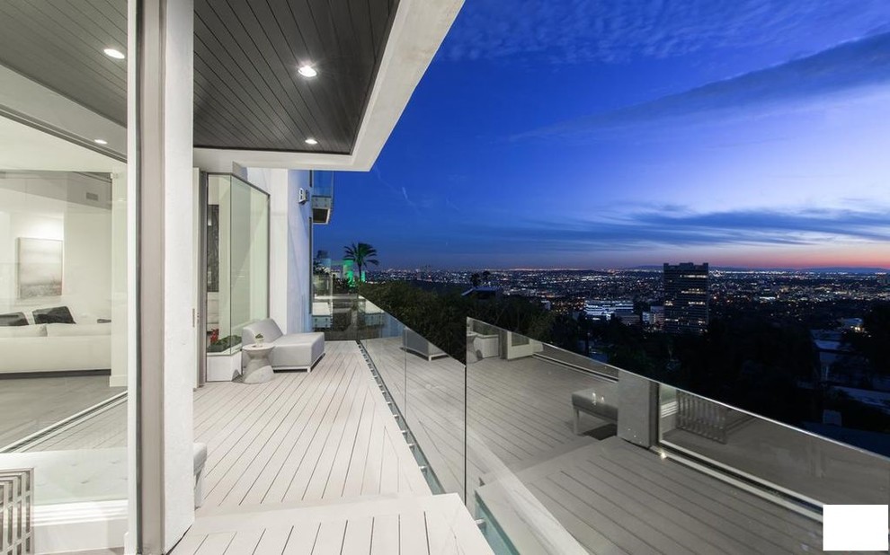 Photo of a mid-sized modern balcony in Los Angeles with a roof extension and glass railing.
