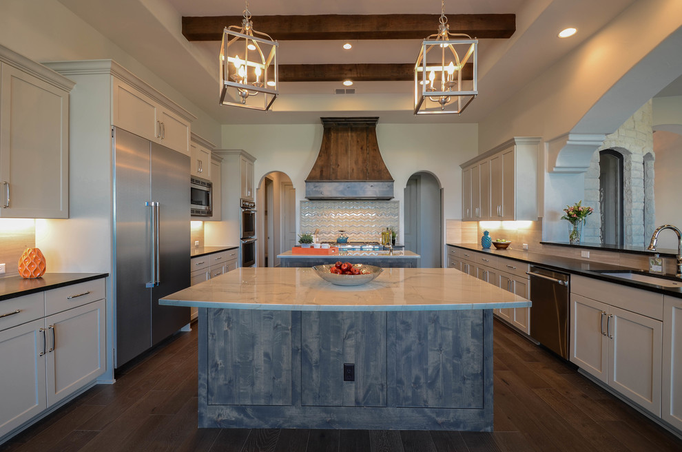 This is an example of an expansive mediterranean u-shaped open plan kitchen in Austin with a single-bowl sink, shaker cabinets, grey cabinets, marble benchtops, beige splashback, glass tile splashback, stainless steel appliances, medium hardwood floors, multiple islands and brown floor.