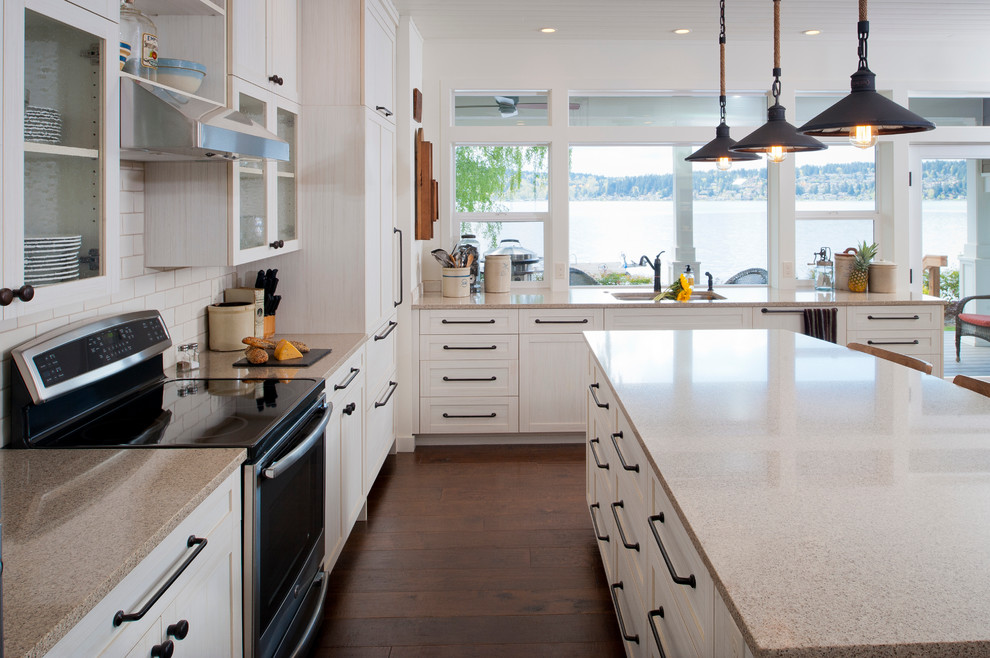 Expansive beach style single-wall open plan kitchen in Seattle with a farmhouse sink, flat-panel cabinets, grey cabinets, quartz benchtops, white splashback, ceramic splashback, white appliances, dark hardwood floors and with island.