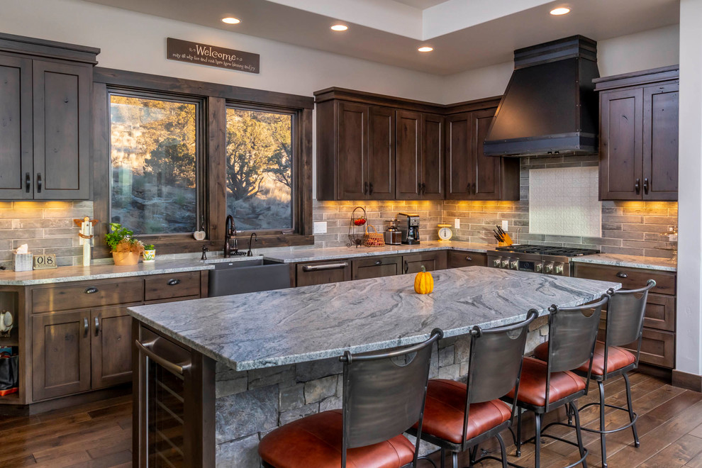 Inspiration for a rustic l-shaped dark wood floor and brown floor kitchen remodel with a farmhouse sink, shaker cabinets, dark wood cabinets, gray backsplash, stainless steel appliances, an island and gray countertops