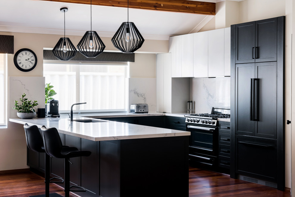 Design ideas for a transitional u-shaped kitchen in Perth with an undermount sink, shaker cabinets, black cabinets, white splashback, stone slab splashback, black appliances, dark hardwood floors, a peninsula, brown floor, white benchtop and vaulted.