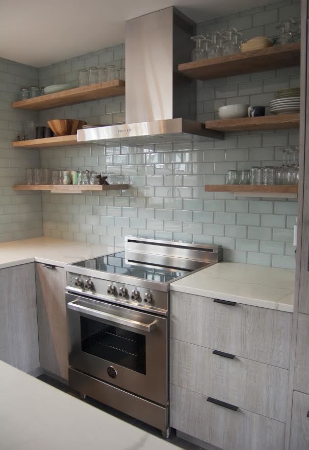 Inspiration for a mid-sized beach style l-shaped eat-in kitchen in Boston with flat-panel cabinets, light wood cabinets, quartzite benchtops, grey splashback, glass tile splashback, stainless steel appliances and with island.