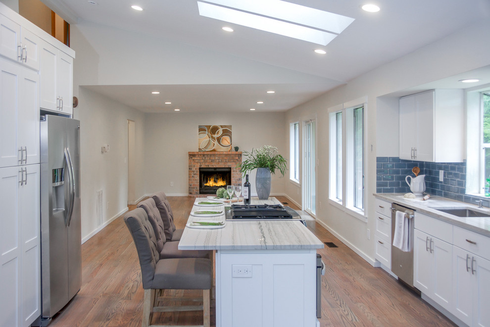 Example of a large transitional galley medium tone wood floor and brown floor open concept kitchen design in Seattle with an undermount sink, shaker cabinets, white cabinets, quartz countertops, blue backsplash, subway tile backsplash, stainless steel appliances, an island and multicolored countertops