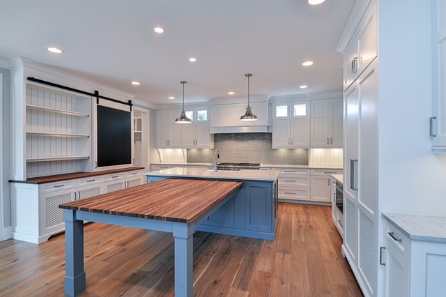 Example of a transitional u-shaped light wood floor kitchen design in Chicago with a farmhouse sink, beaded inset cabinets, white cabinets, quartz countertops, gray backsplash, glass tile backsplash, paneled appliances and an island