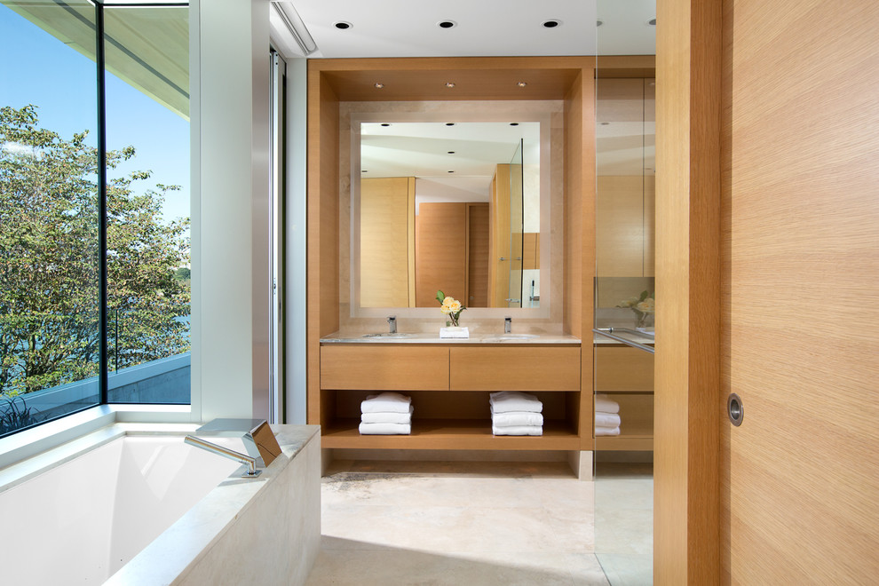 Design ideas for a contemporary master bathroom in Vancouver with an undermount sink, flat-panel cabinets, light wood cabinets, limestone benchtops, a drop-in tub, a curbless shower, a wall-mount toilet and travertine floors.