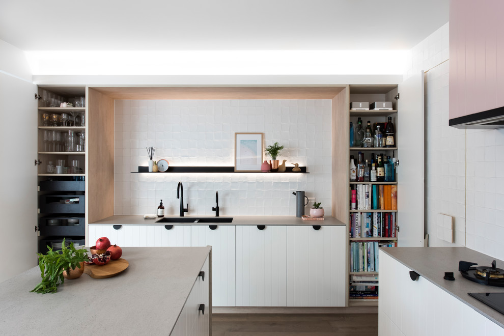 Photo of a mid-sized contemporary l-shaped open plan kitchen in Sydney with a double-bowl sink, white cabinets, recycled glass benchtops, white splashback, cement tile splashback, black appliances, medium hardwood floors, with island and grey benchtop.