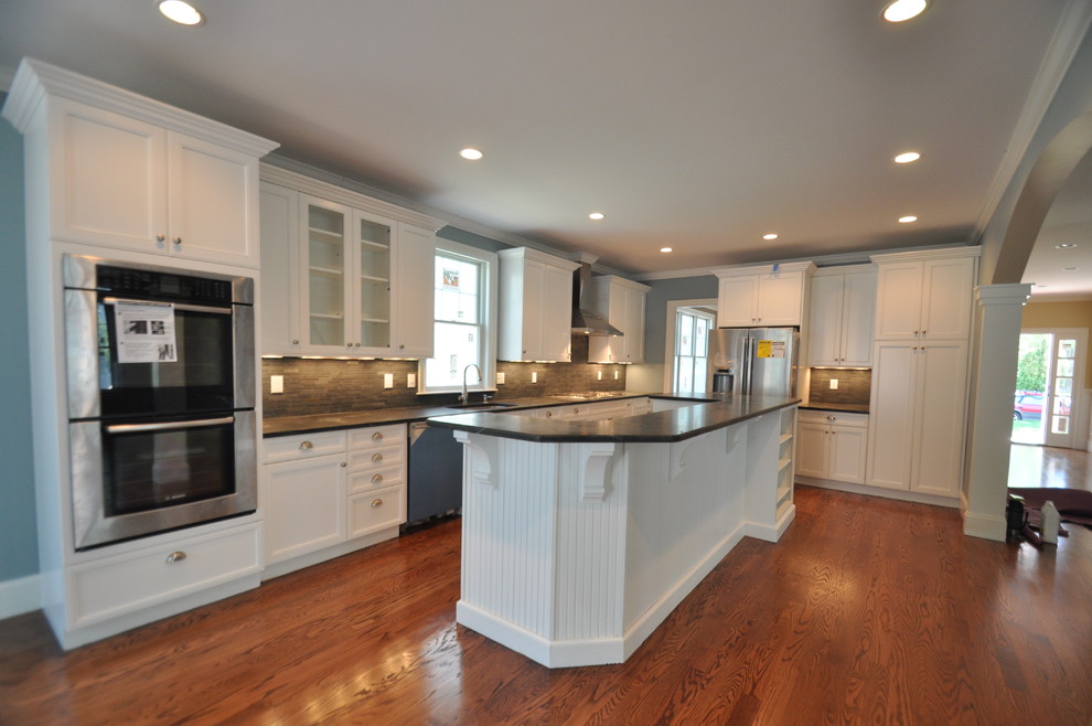 Photo of a large traditional l-shaped open plan kitchen in Boston with shaker cabinets, white cabinets, with island, an undermount sink, brown splashback, matchstick tile splashback, stainless steel appliances, medium hardwood floors and blue floor.