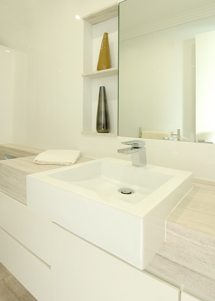 This is an example of a mid-sized modern master bathroom in Sydney with flat-panel cabinets, white cabinets, a drop-in tub, an alcove shower, a one-piece toilet, white tile, ceramic tile, white walls, limestone floors, a vessel sink, limestone benchtops, beige floor, an open shower, beige benchtops, a niche, a single vanity, a floating vanity, recessed and decorative wall panelling.