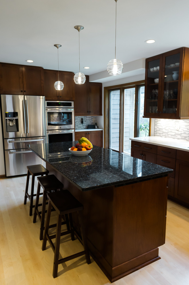 Large transitional l-shaped light wood floor eat-in kitchen photo with an undermount sink, shaker cabinets, dark wood cabinets, quartz countertops, gray backsplash, matchstick tile backsplash, stainless steel appliances and an island