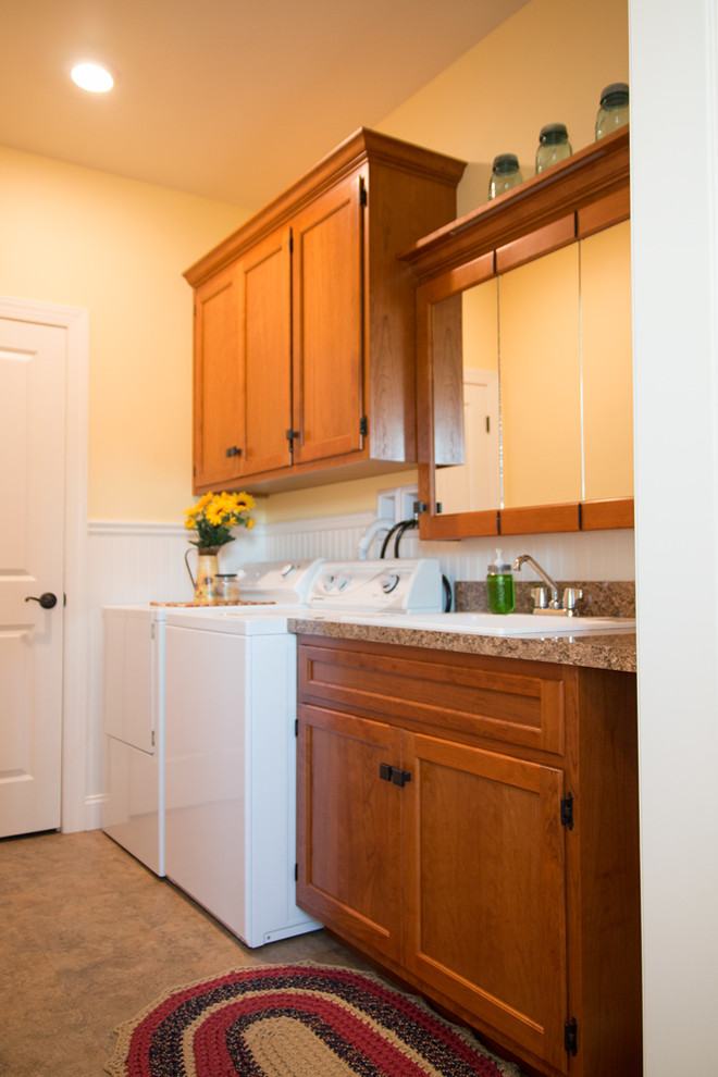 Design ideas for a mid-sized country single-wall dedicated laundry room in Philadelphia with a drop-in sink, shaker cabinets, medium wood cabinets, laminate benchtops, yellow walls, laminate floors, a side-by-side washer and dryer and beige floor.