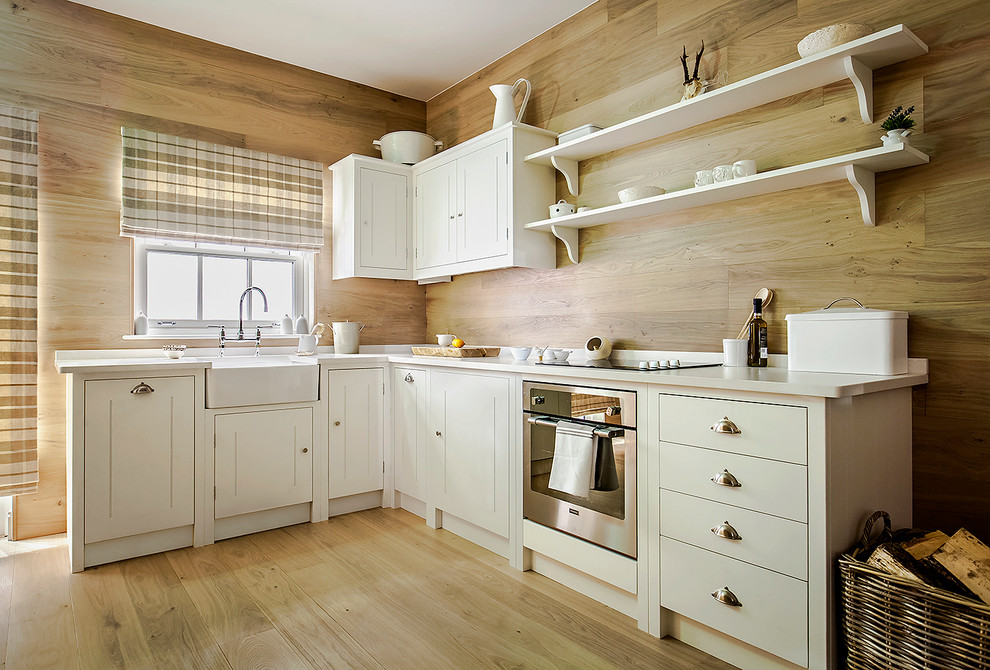 Design ideas for a small country l-shaped kitchen in London with a farmhouse sink, beaded inset cabinets, white cabinets, stainless steel appliances and light hardwood floors.