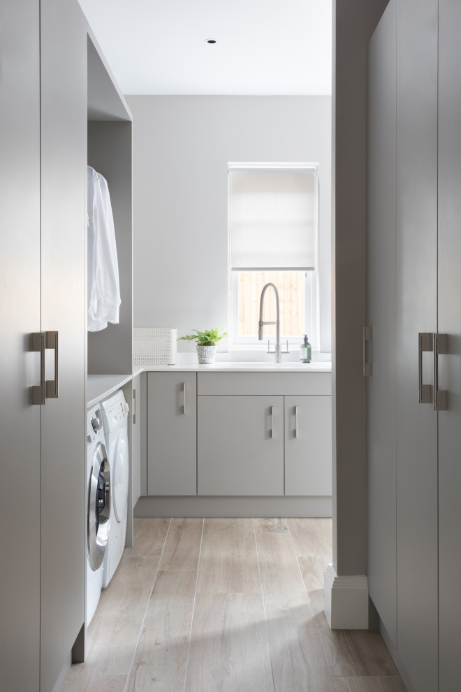 Inspiration for an expansive contemporary laundry room in Surrey with an integrated sink, flat-panel cabinets, grey cabinets, quartzite benchtops, porcelain floors, grey floor and white benchtop.