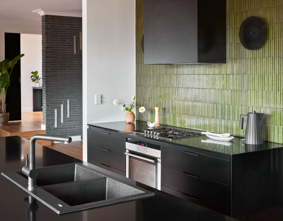 Mid-sized contemporary kitchen in Melbourne with a double-bowl sink, flat-panel cabinets, black cabinets, solid surface benchtops, green splashback, mosaic tile splashback, stainless steel appliances, with island and black benchtop.