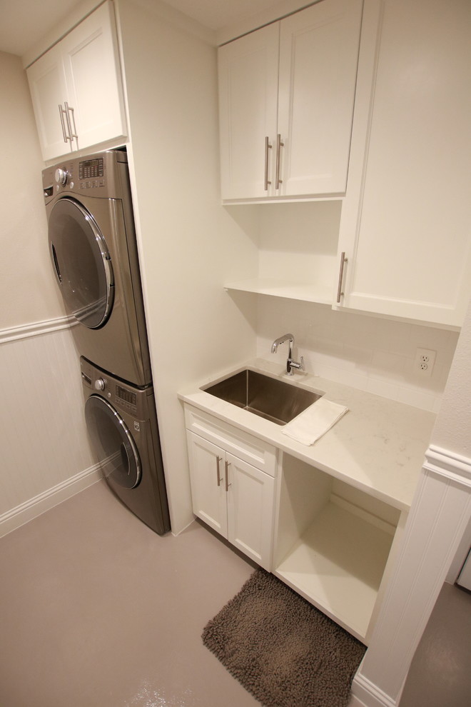 Large traditional single-wall dedicated laundry room in Houston with an undermount sink, shaker cabinets, white cabinets, granite benchtops, beige walls, concrete floors, a stacked washer and dryer and grey floor.