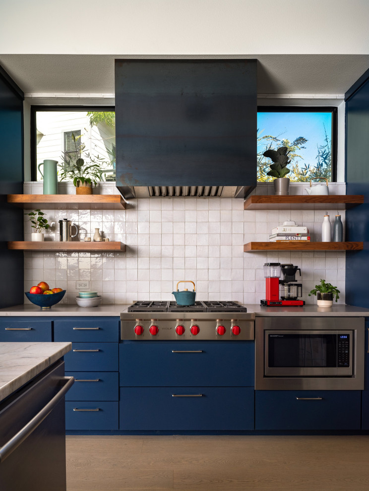 Inspiration for a large contemporary u-shaped open plan kitchen in Austin with a submerged sink, flat-panel cabinets, blue cabinets, quartz worktops, white splashback, terracotta splashback, stainless steel appliances, light hardwood flooring, an island, grey worktops and a drop ceiling.