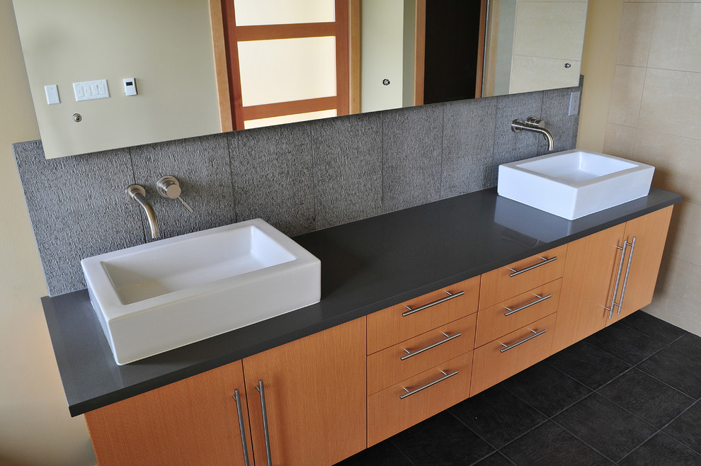 This is an example of a large contemporary bathroom in Seattle with a vessel sink, flat-panel cabinets, medium wood cabinets, solid surface benchtops, an alcove tub, black tile, stone tile, beige walls and slate floors.