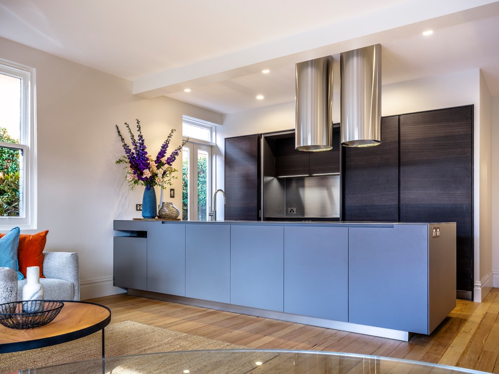 This is an example of a contemporary open plan kitchen in Sydney with flat-panel cabinets, blue cabinets, light hardwood floors, a peninsula and beige floor.