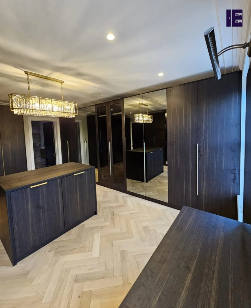Immagine di una grande cabina armadio minimalista con ante di vetro, ante in legno bruno e pavimento in compensato