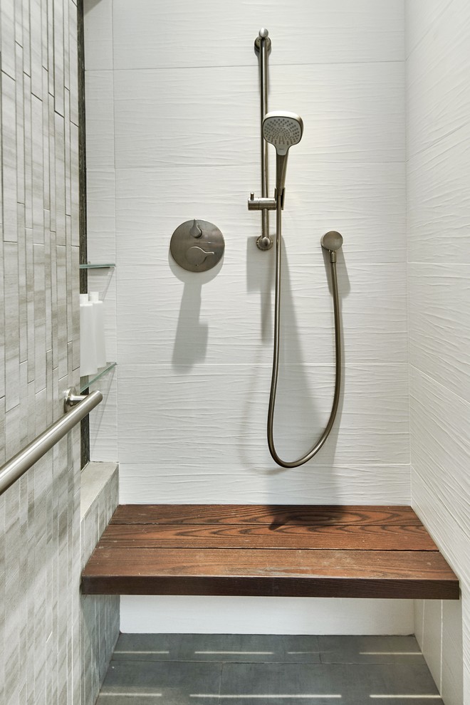 Photo of a mid-sized transitional master bathroom in San Francisco with shaker cabinets, medium wood cabinets, a curbless shower, a wall-mount toilet, white tile, ceramic tile, grey walls, ceramic floors, granite benchtops, grey floor, a hinged shower door, black benchtops, a trough sink and a shower seat.